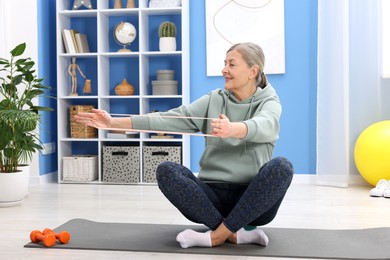 Smiling elderly woman exercising with fitness elastic band at home