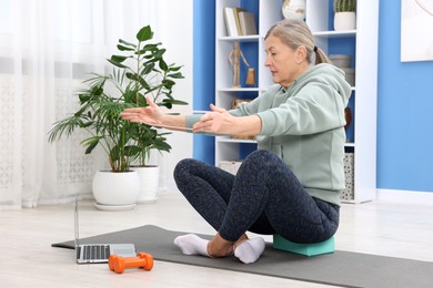 Photo of Elderly woman exercising with fitness elastic band near laptop at home