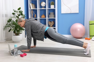 Elderly woman exercising near laptop at home