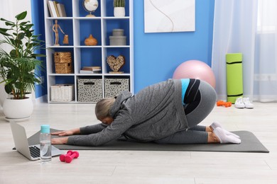 Elderly woman exercising near laptop at home