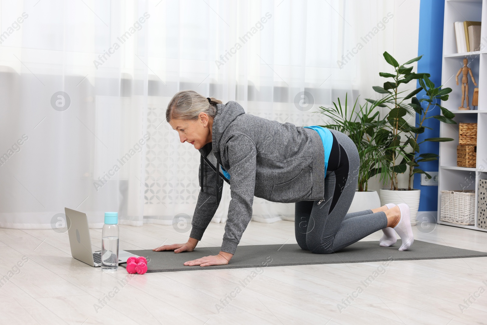 Photo of Elderly woman exercising near laptop at home