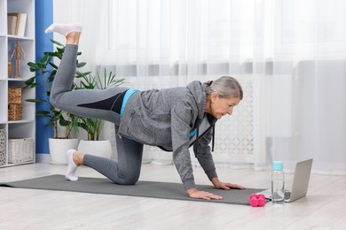 Elderly woman exercising near laptop at home