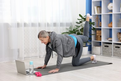 Elderly woman exercising near laptop at home