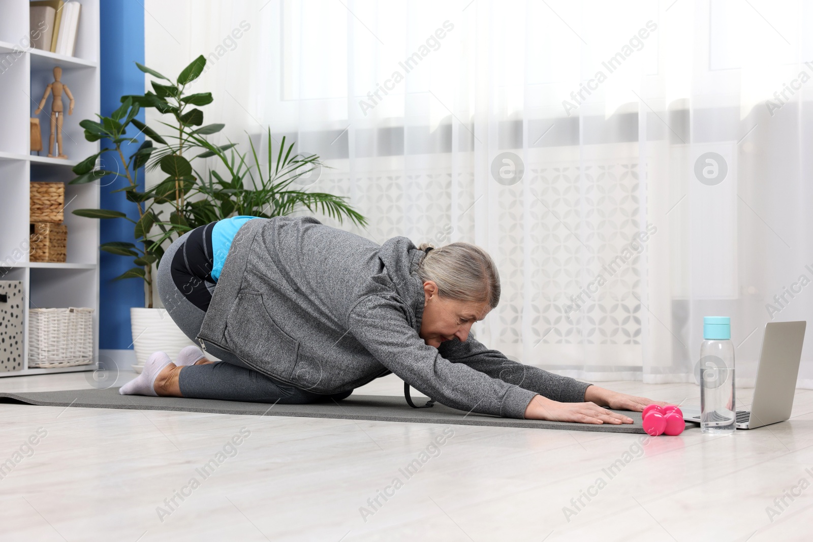 Photo of Elderly woman exercising near laptop at home