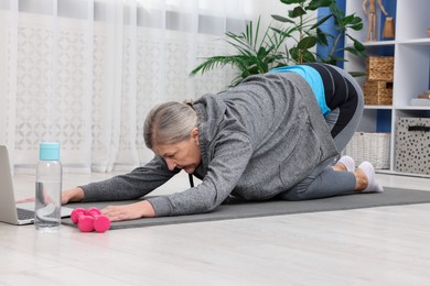 Elderly woman exercising near laptop at home