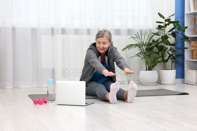 Elderly woman exercising near laptop at home