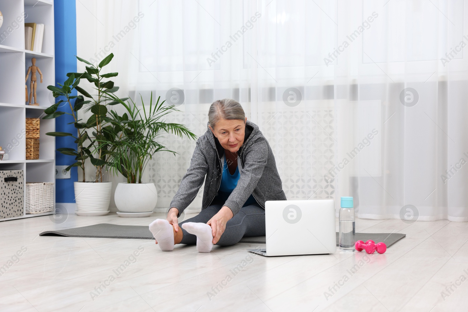 Photo of Elderly woman exercising near laptop at home