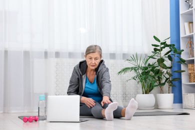 Photo of Elderly woman exercising near laptop at home