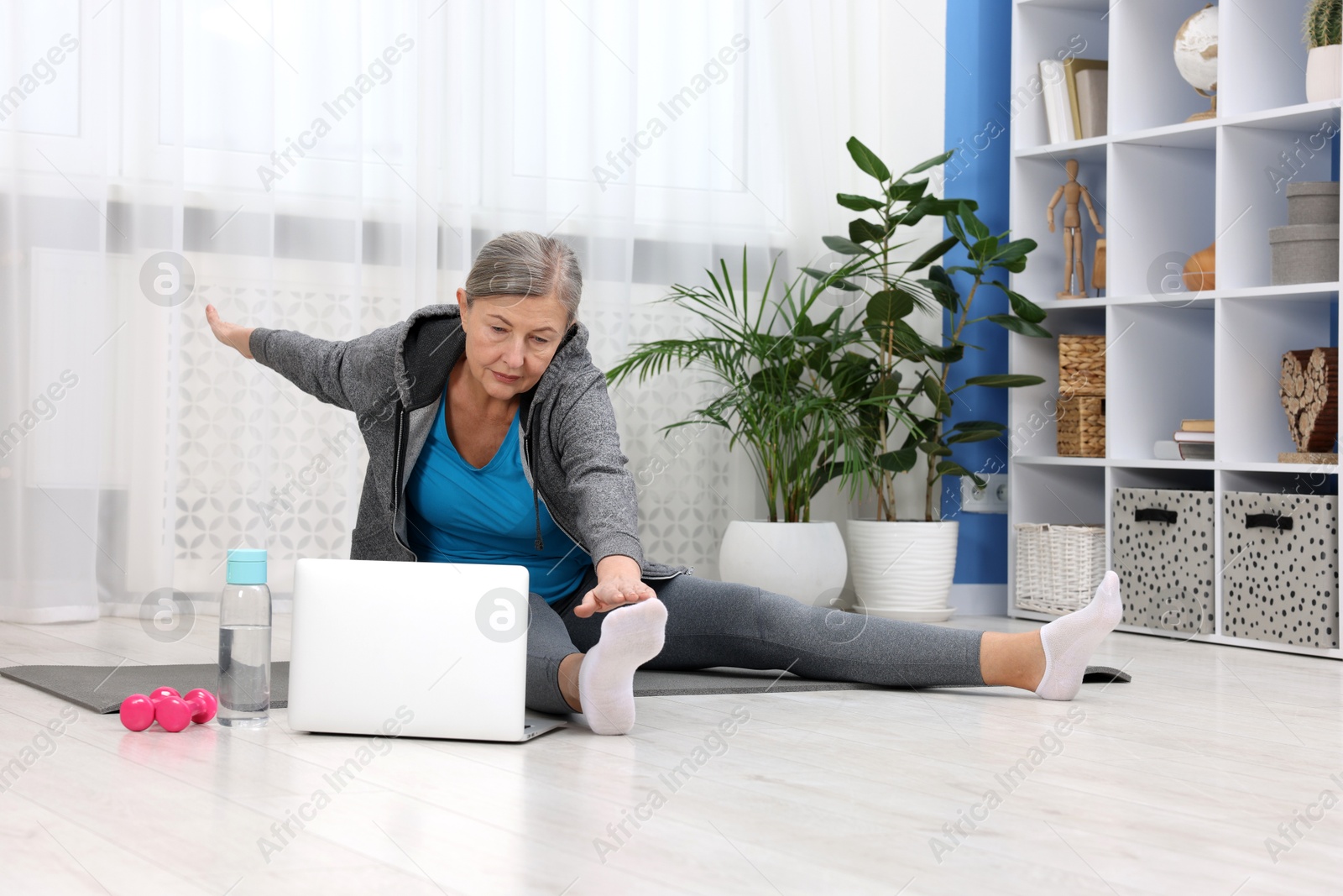 Photo of Elderly woman exercising near laptop at home