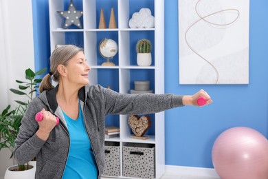 Smiling elderly woman exercising with dumbbells at home