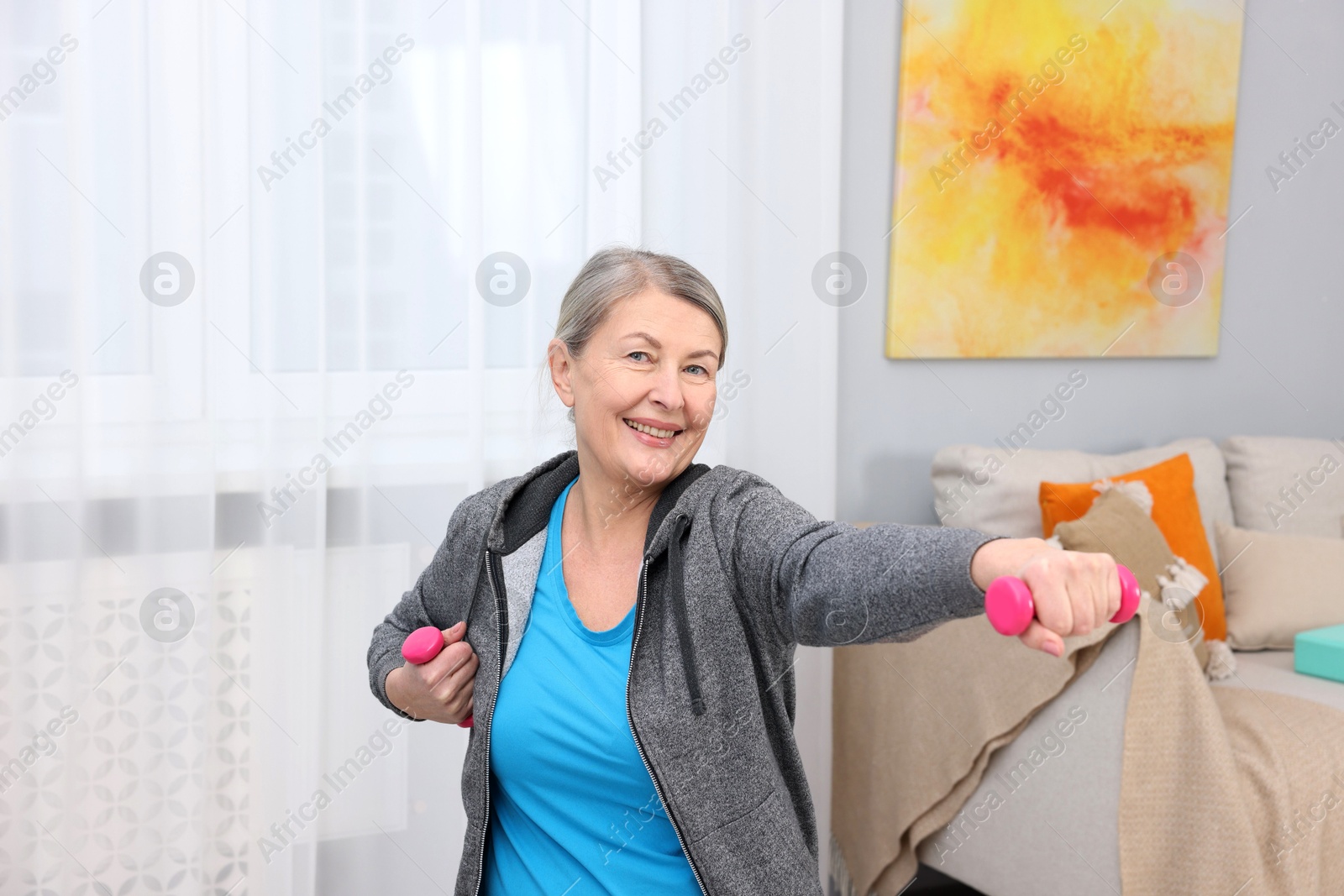 Photo of Smiling elderly woman exercising with dumbbells at home