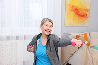 Smiling elderly woman exercising with dumbbells at home