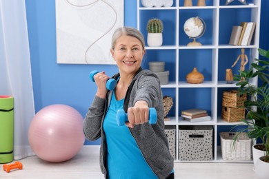 Smiling elderly woman exercising with dumbbells at home