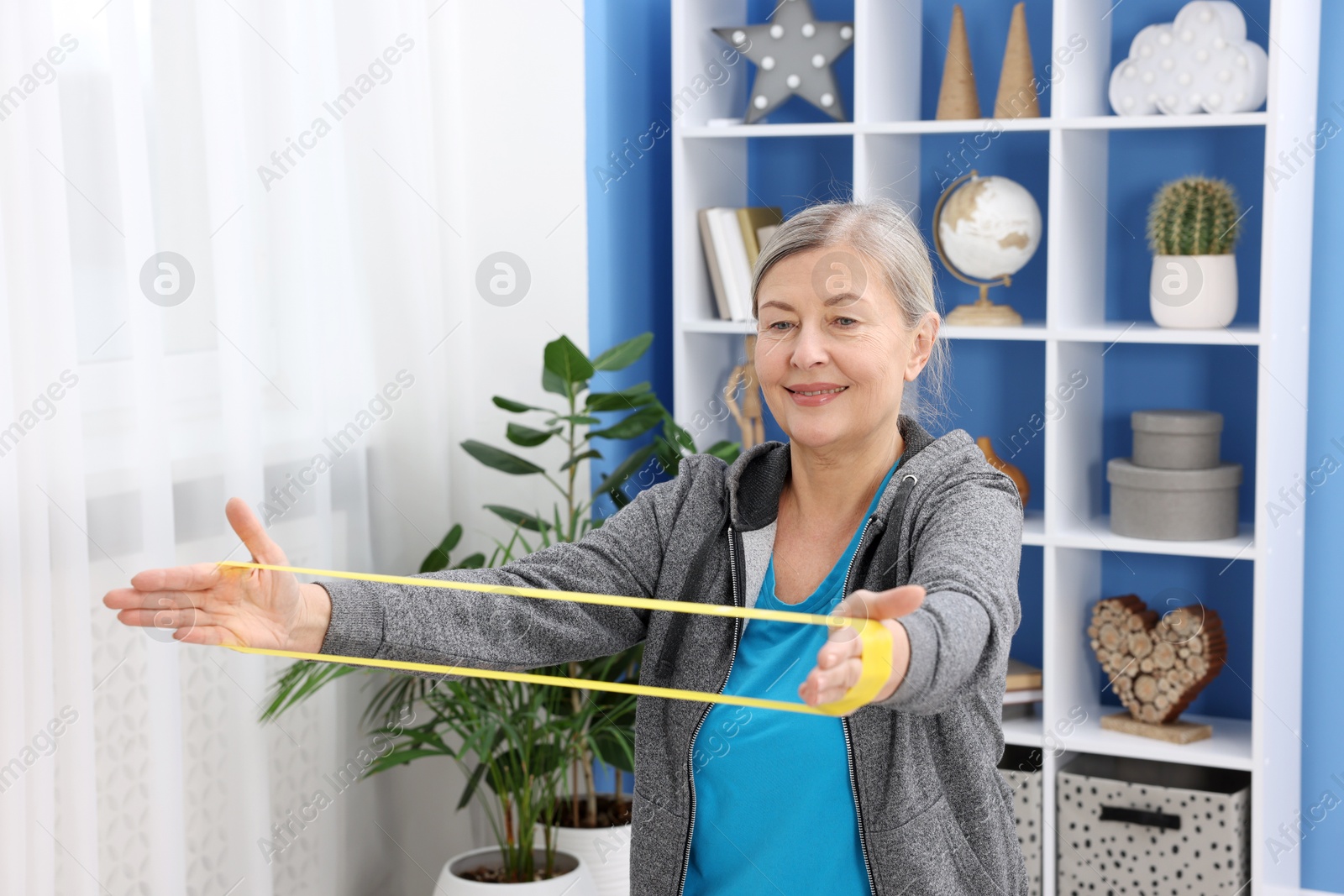 Photo of Smiling elderly woman exercising with fitness elastic band at home