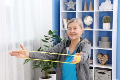 Smiling elderly woman exercising with fitness elastic band at home