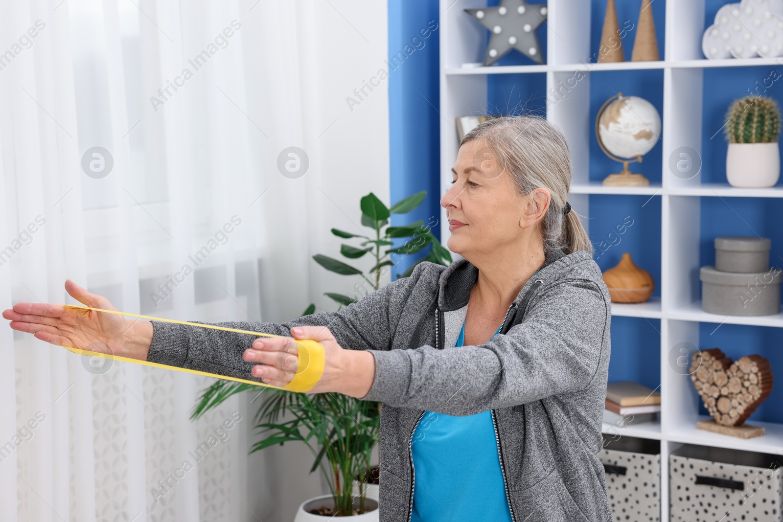 Photo of Elderly woman exercising with fitness elastic band at home