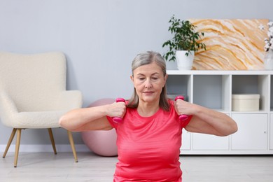 Photo of Elderly woman exercising with dumbbells at home