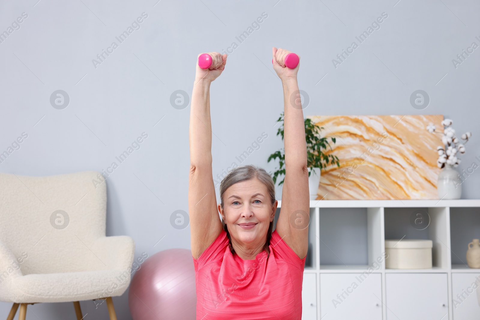 Photo of Elderly woman exercising with dumbbells at home