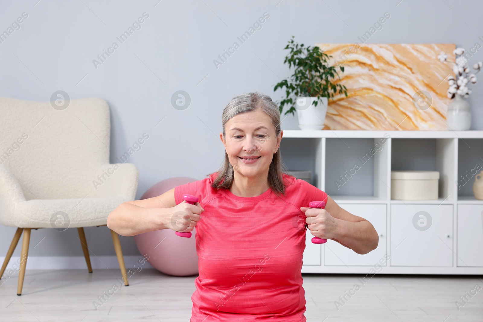 Photo of Smiling elderly woman exercising with dumbbells at home