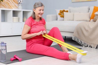 Photo of Smiling elderly woman exercising with fitness elastic band at home