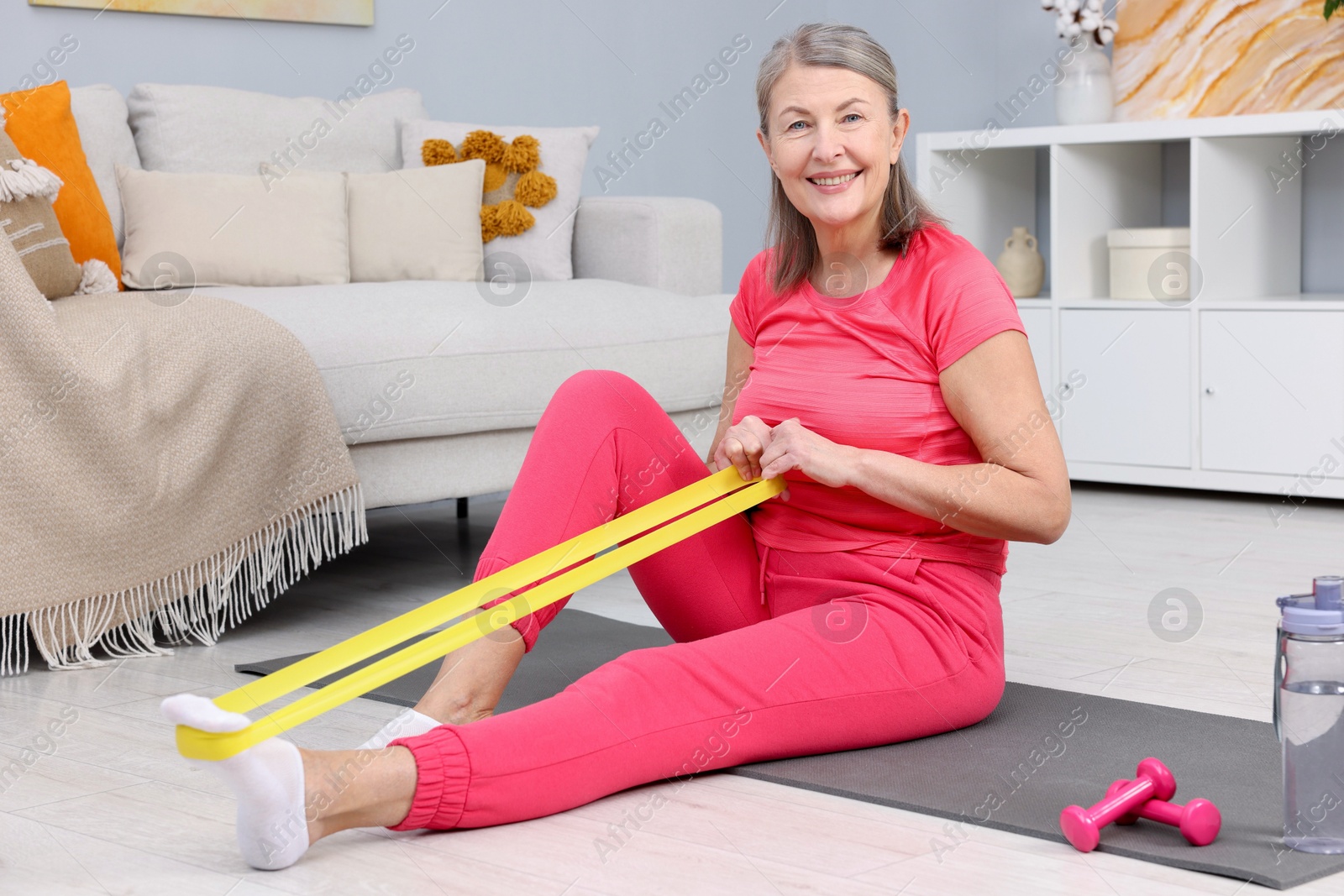 Photo of Smiling elderly woman exercising with fitness elastic band at home