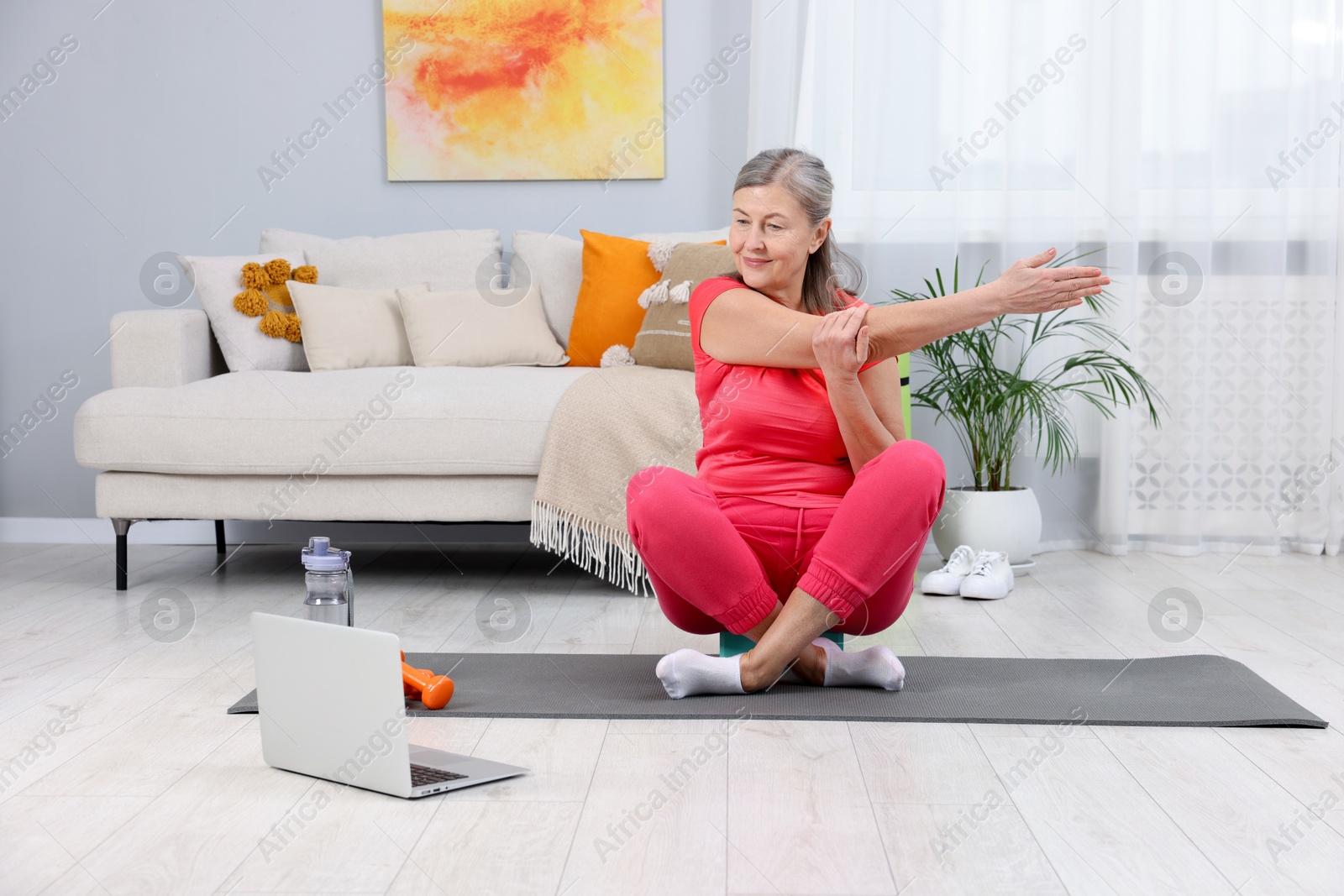 Photo of Elderly woman exercising near laptop at home