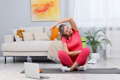 Photo of Smiling elderly woman exercising near laptop at home