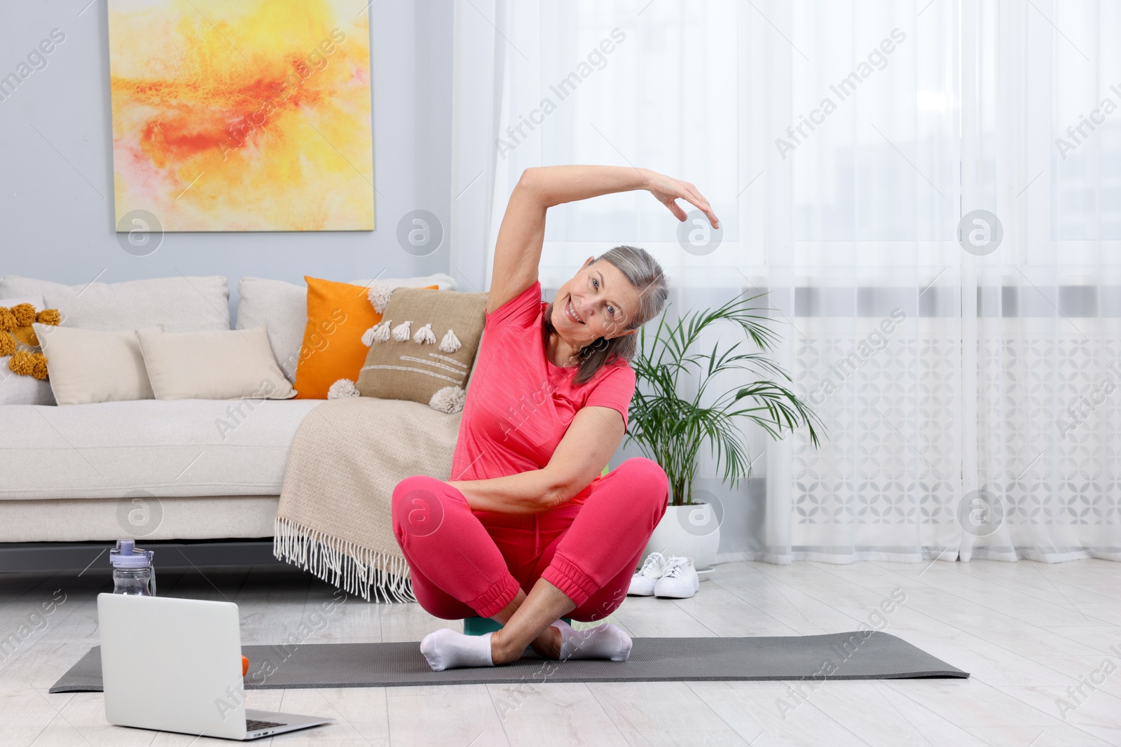 Photo of Smiling elderly woman exercising near laptop at home