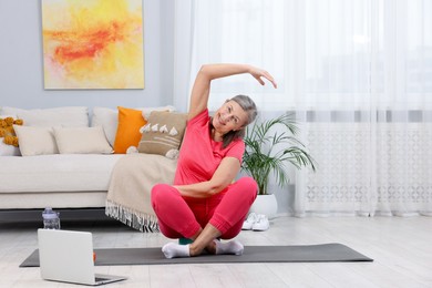 Smiling elderly woman exercising near laptop at home