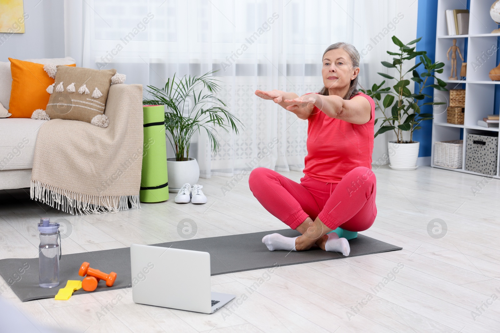 Photo of Elderly woman exercising near laptop at home