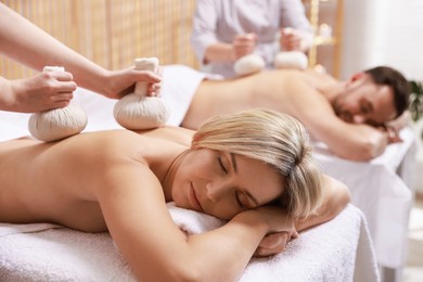 Couple receiving relaxing massage with herbal bags in spa salon, selective focus