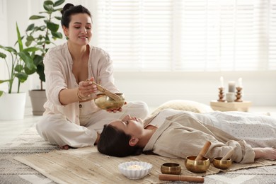 Woman undergoing singing bowl therapy lying on floor indoors. Space for text