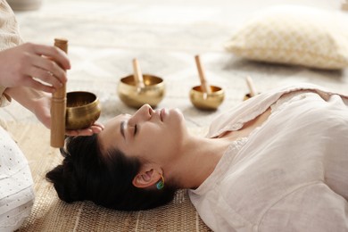 Woman undergoing singing bowl therapy lying on floor indoors