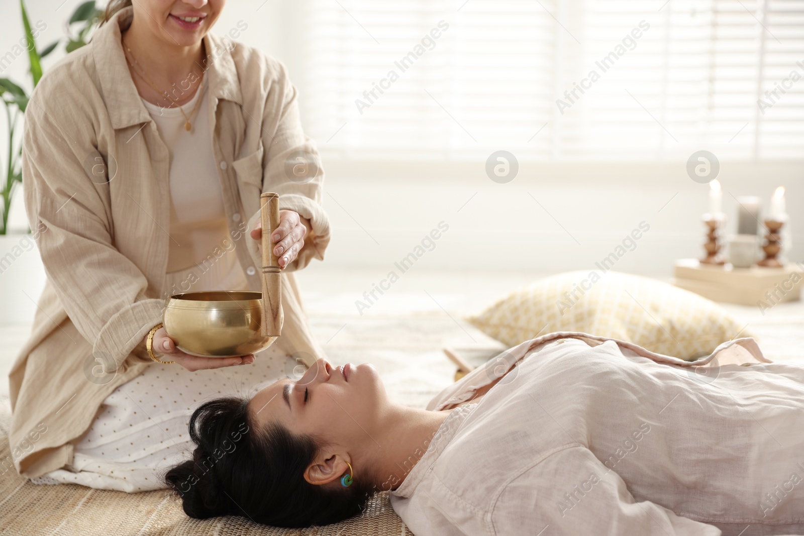 Photo of Woman undergoing singing bowl therapy lying on floor indoors. Space for text