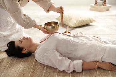 Woman undergoing singing bowl therapy lying on floor indoors