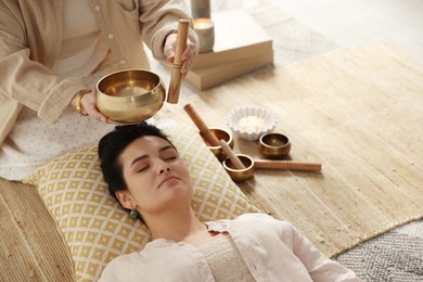 Woman undergoing singing bowl therapy lying on floor indoors