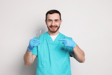 Professional dentist pointing at tools on light background