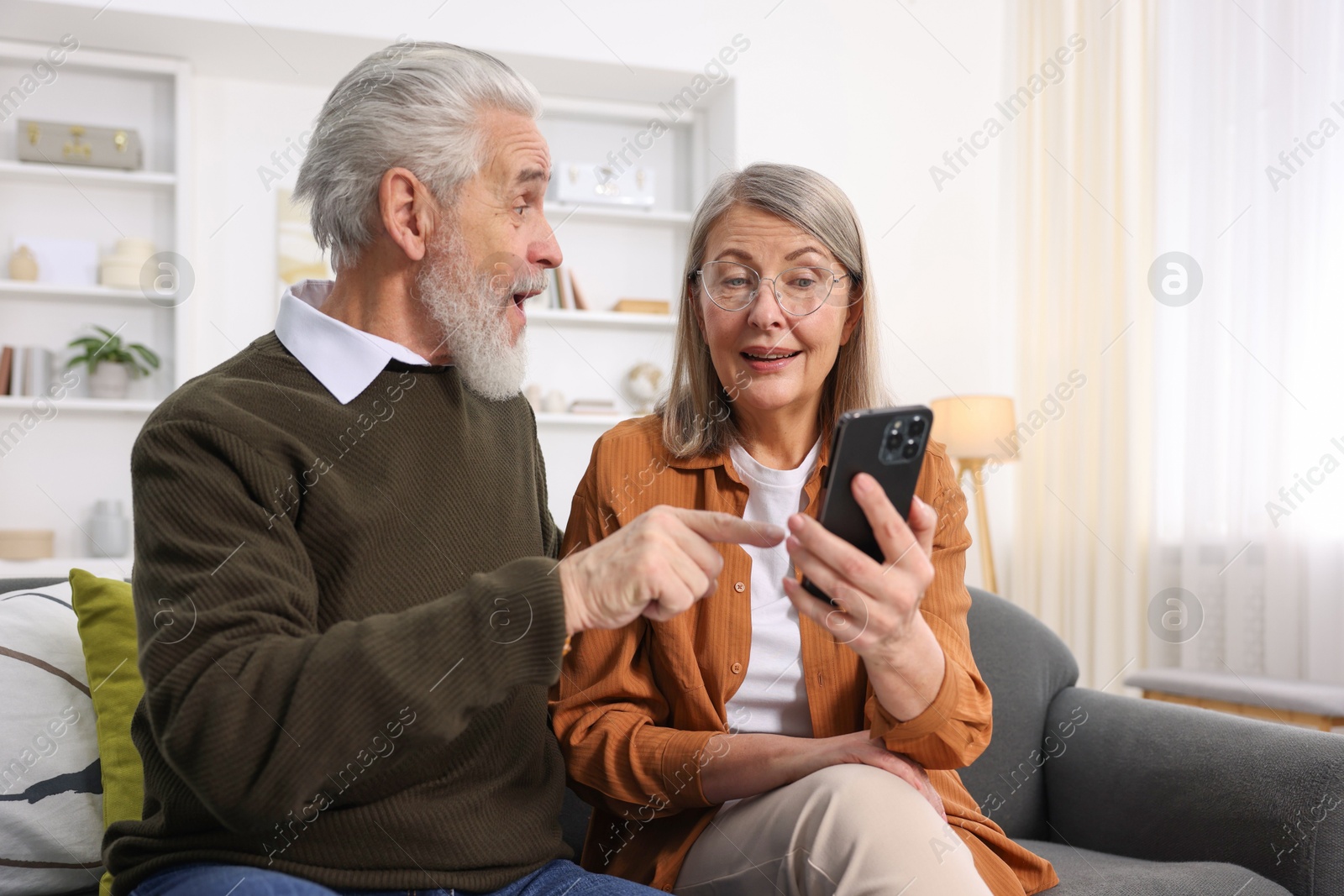 Photo of Happy elderly couple with smartphone on sofa at home