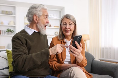 Happy elderly couple with smartphone on sofa at home