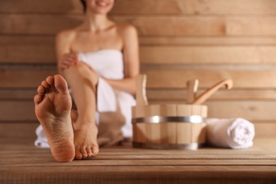 Smiling woman relaxing on bench with bath supplies at sauna, closeup. Selective focus