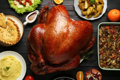 Whole baked turkey and other dishes served on black wooden table, flat lay