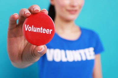 Photo of Woman showing red button badge with word Volunteer on light blue background, closeup