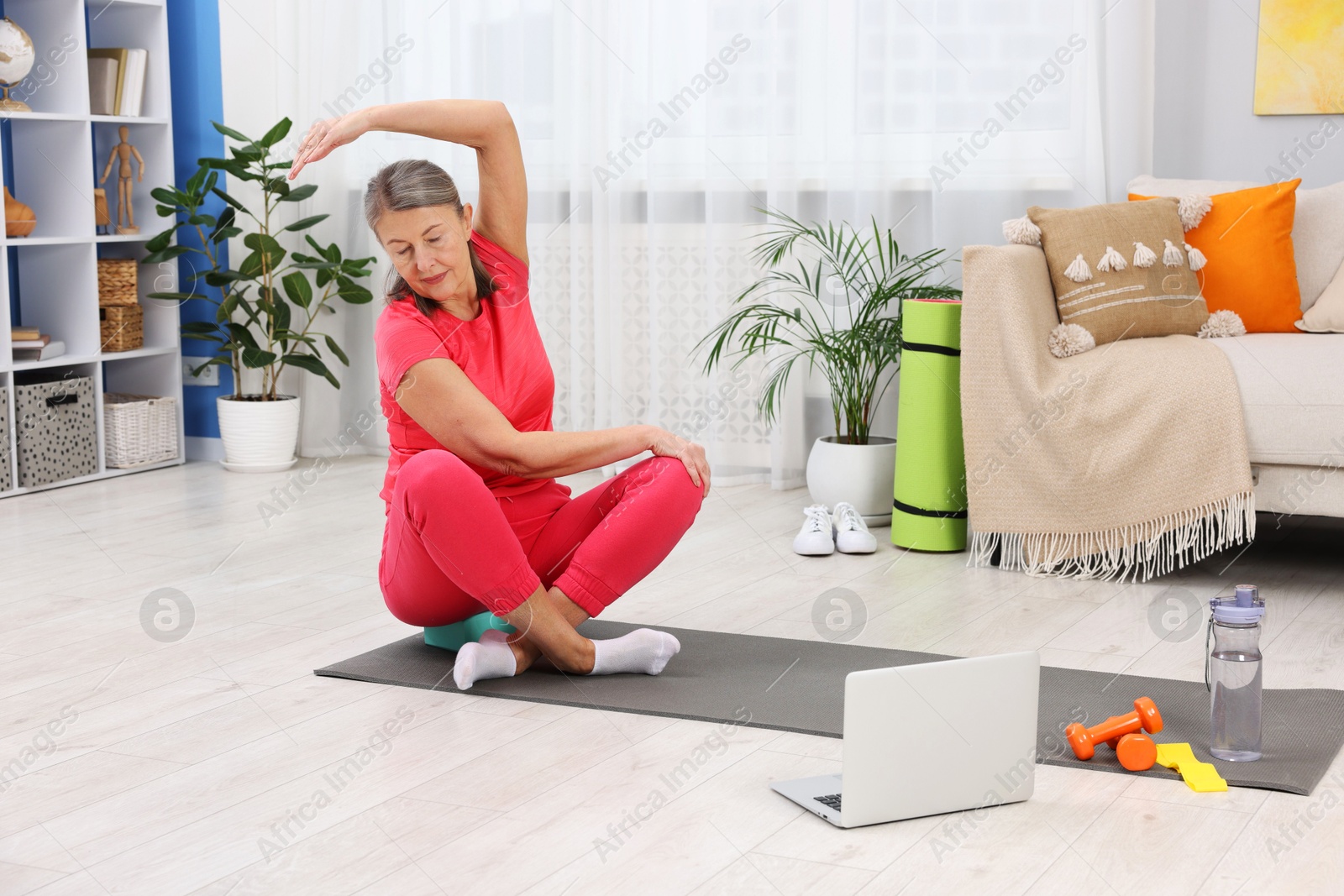 Photo of Elderly woman exercising near laptop at home