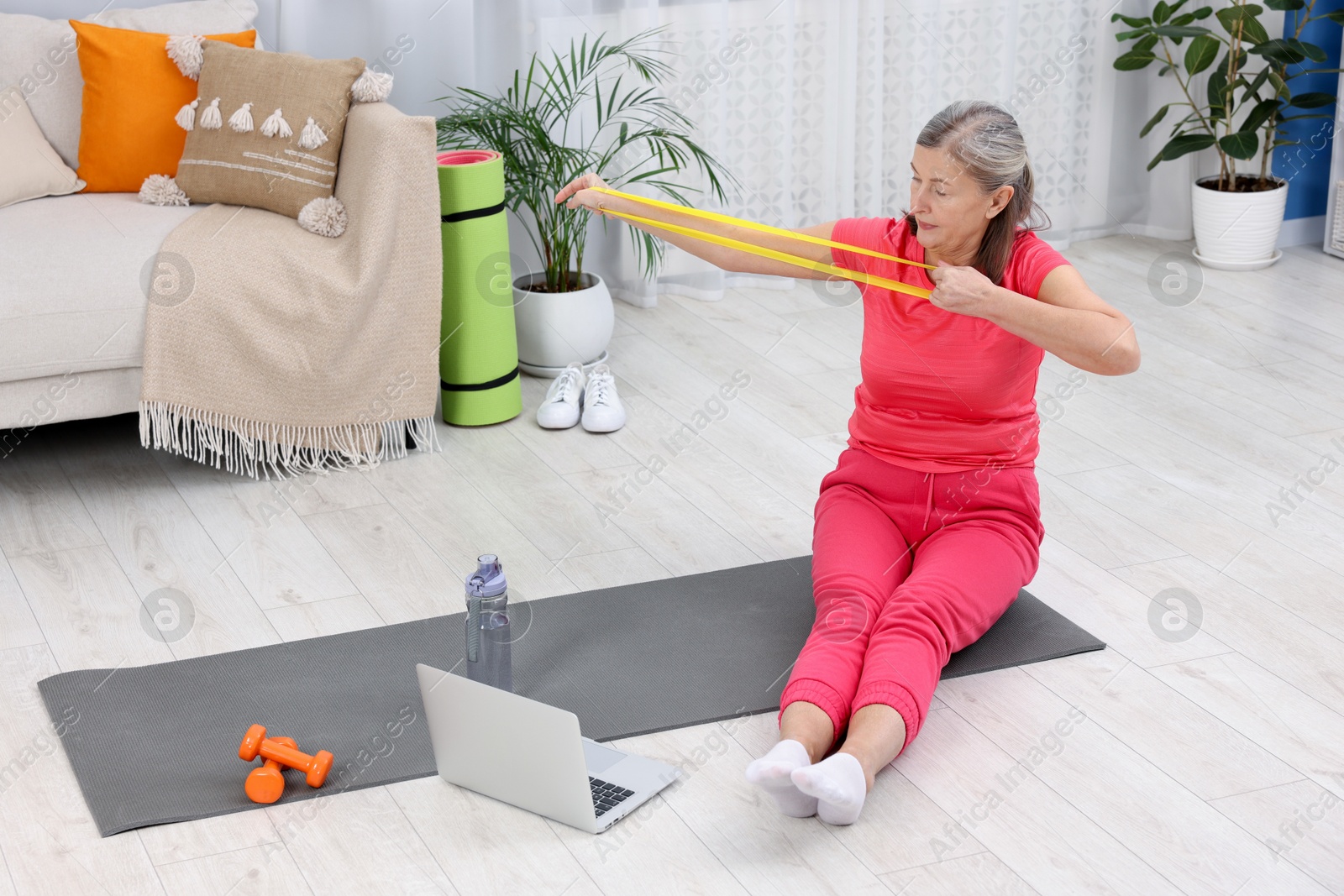 Photo of Elderly woman exercising with fitness elastic band near laptop at home