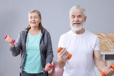 Photo of Smiling elderly couple exercising with dumbbells at home