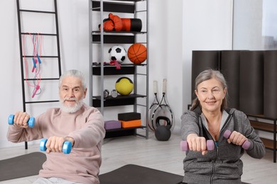 Smiling elderly couple exercising with dumbbells at home