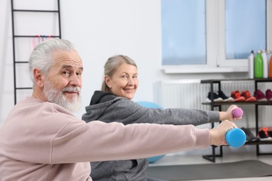 Photo of Smiling elderly couple exercising with dumbbells at home