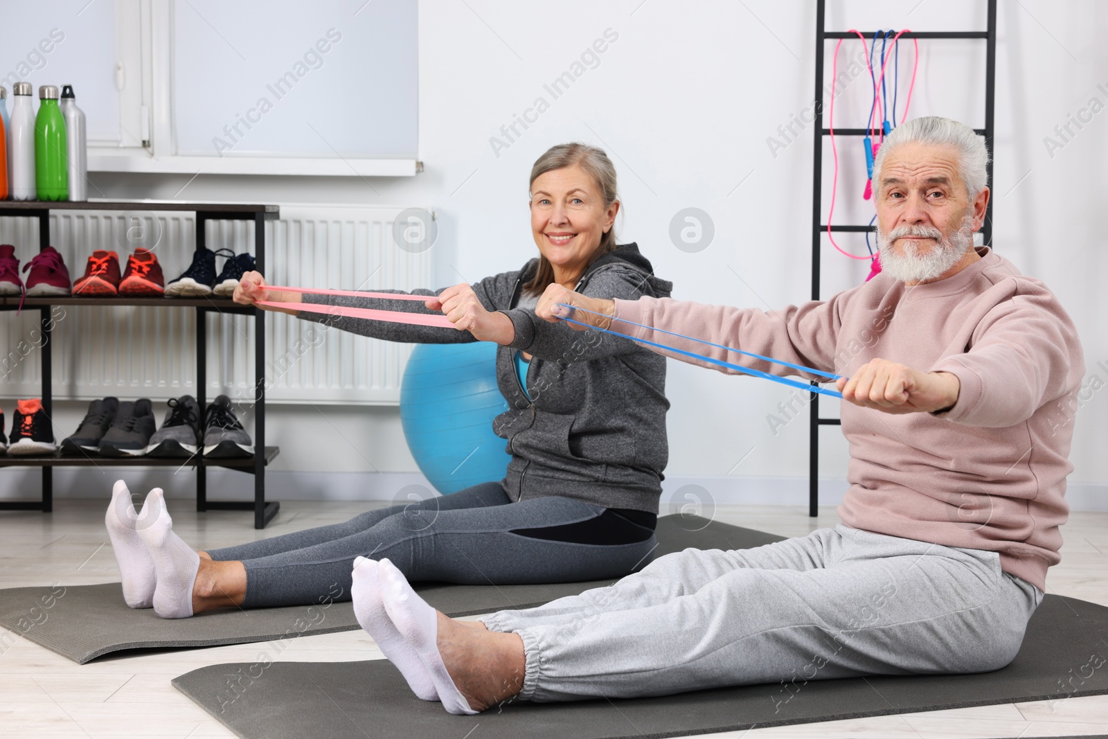 Photo of Smiling elderly couple exercising with fitness elastic bands at home