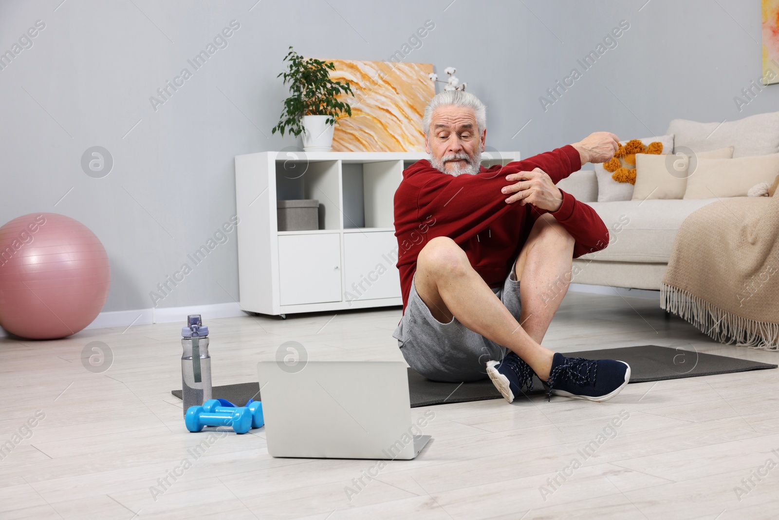 Photo of Elderly man exercising near laptop at home