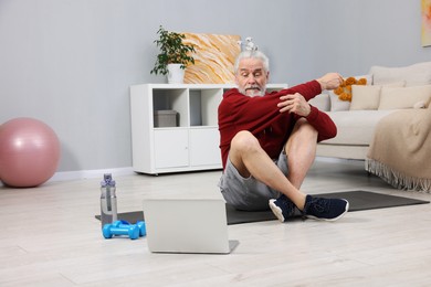 Elderly man exercising near laptop at home